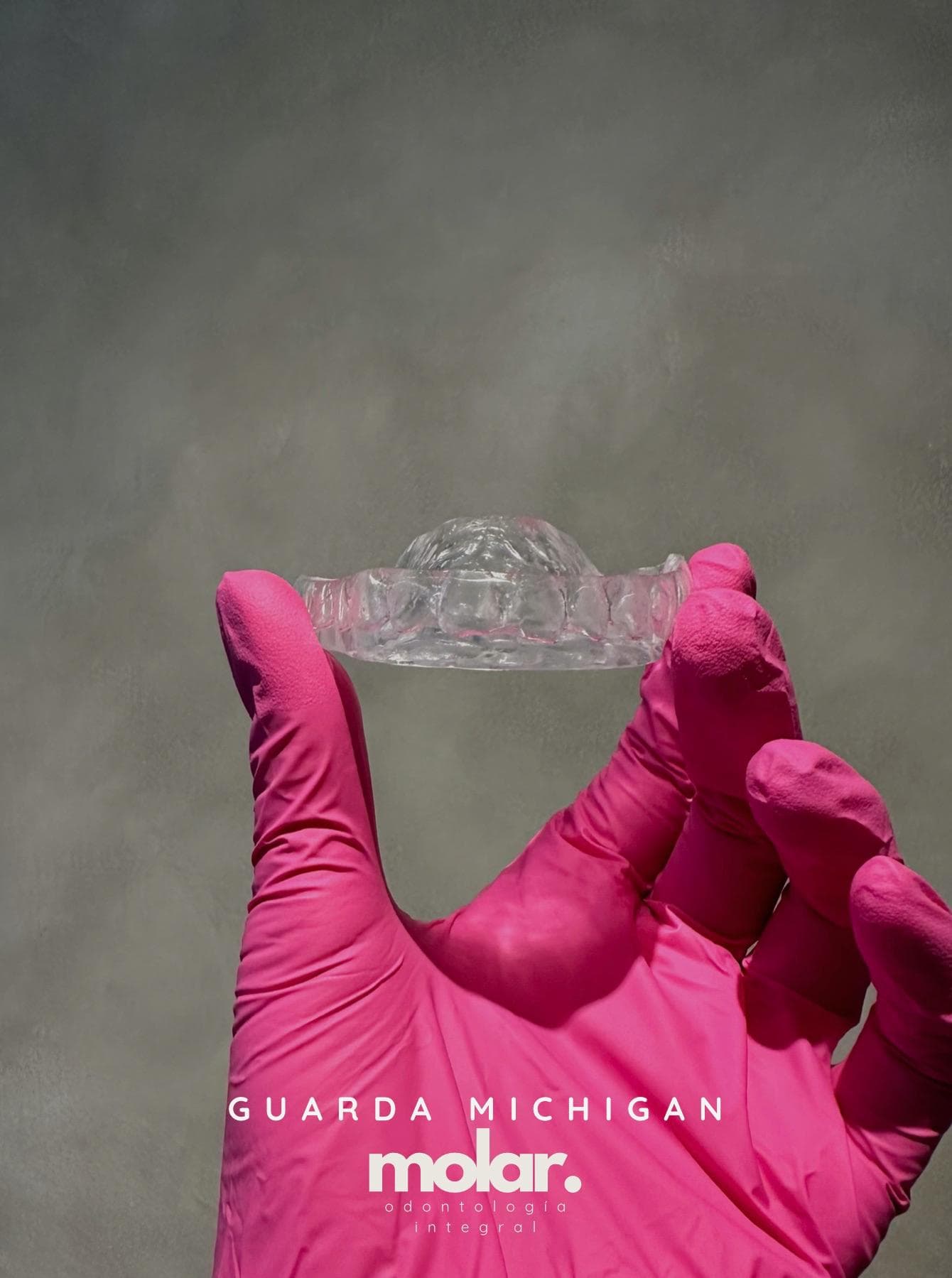 Guarda tipo Michigan de acrílico transparente sostenida con guante rosa, con el rótulo del consultorio